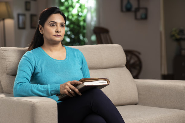 一个女人拿着日记坐在家里的沙发上。:库存图片图片下载