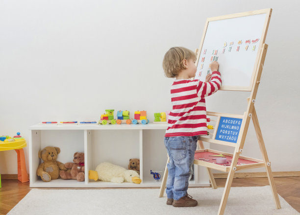 可爱的小孩在磁性板上玩耍，在家里学习字母、数字和几何形状。教育和有趣的室内活动，为早期发展。图片下载