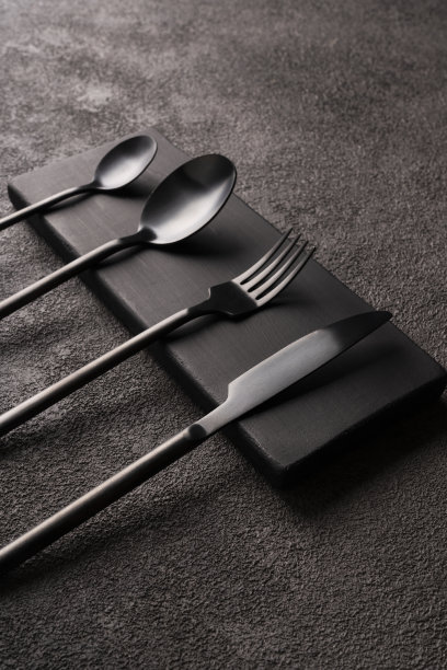 黑色哑光餐具，叉子，勺子，刀，在深色混凝土上。简约的静物，时尚的餐具。垂直的特写照片图片下载