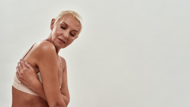 自我保健。一个快乐美丽的白人成熟女人的肖像在内衣拥抱自己，而摆出半裸在工作室的灯光背景图片下载