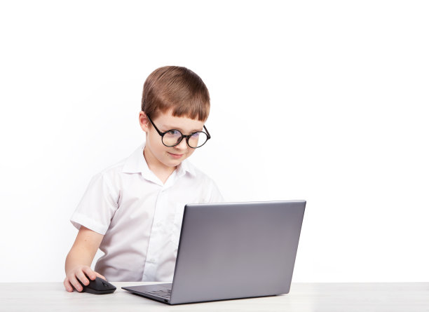 一个戴眼镜的小学生坐在桌子旁，桌上放着一台白色背景的笔记本电脑图片下载