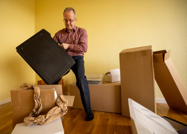 动态强壮的中年男子在空的公寓房间提着一个沉重的手提箱搬进或搬出。到处都是纸箱图片下载