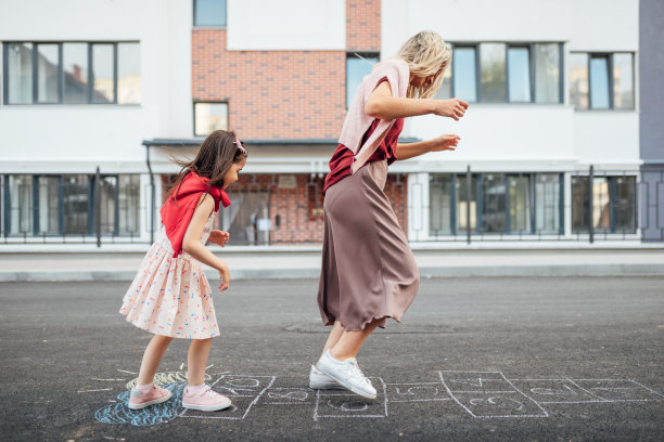 一个快乐的小女孩和她的妈妈在户外的操场上玩跳房子。一个孩子在外面和妈妈玩。一个孩子和妈妈在外面的人行道上玩跳房子游戏。图片下载