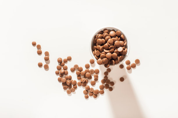 白色背景上的白色一次性杯子里的巧克力小丸子。顶视图特写。平的。调和巧克力糖果的概念。批发的巧克力。图片下载