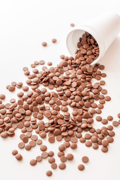 在白色背景上，一次性杯子上散落着巧克力屑。DIY自制的糖果。家庭糖果商的经营理念。顶视图特写。平的。图片下载