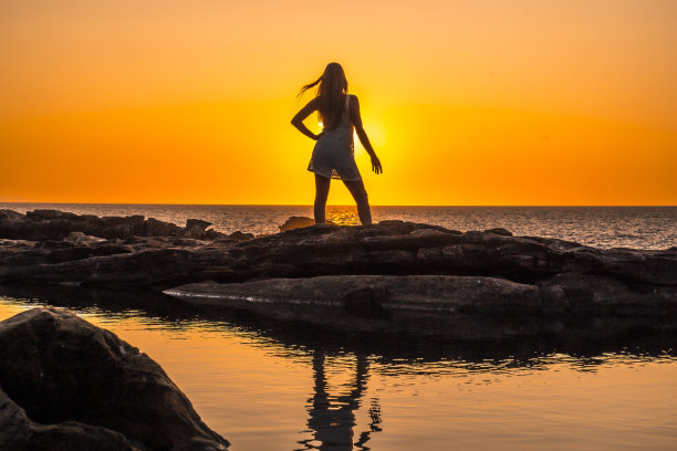 生活方式，一个年轻的金发女郎的剪影在一个橙色的日落白色的裙子图片下载