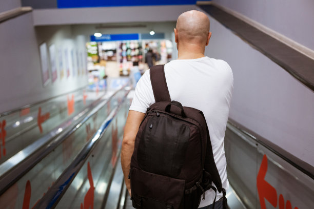 秃头男人背着背包走下自动扶梯去购物中心图片下载