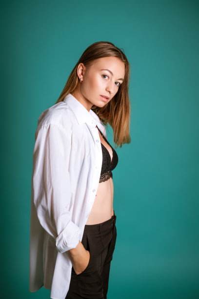 年轻女子在白色衬衫和黑色内衣摆姿势在工作室的蓝色背景图片下载