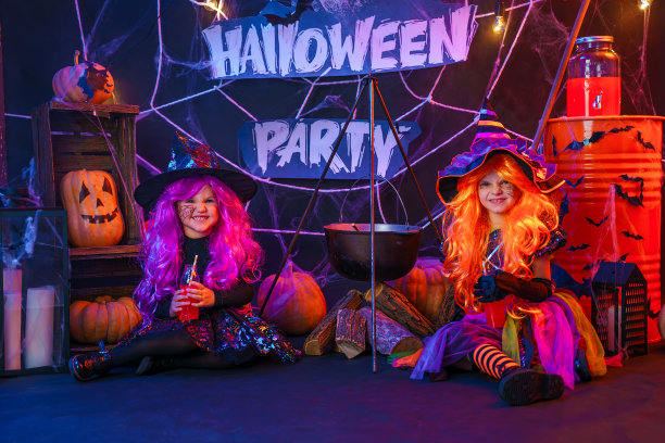 两个漂亮的小女孩穿着女巫的服装在室内用南瓜庆祝快乐的万圣节派对图片下载