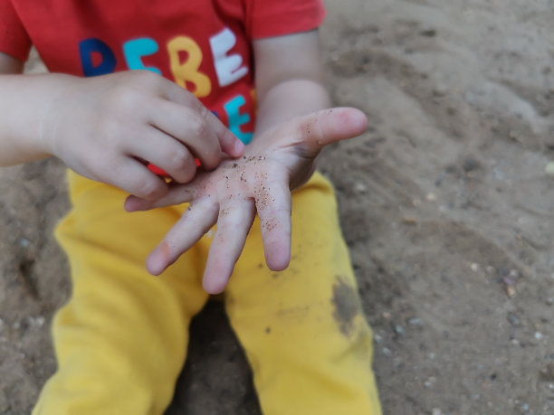 孩子坐在沙箱里，这是孩子的手掌在沙里的特写。图片下载