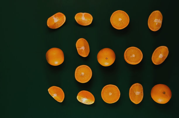 一片片美味的橘子在绿色的背景下平躺着。明亮的橙色薄片在黑暗的背景上，一个对比鲜明的背景吸引注意。图片下载