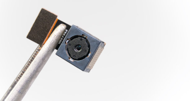 手机摄像模块的特写。在摄影棚里，用特写镊子或夹子夹住智能手机镜头，背景是白色，有拷贝空间。宏图片下载