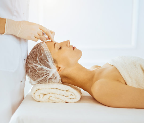 女子接受美容注射与闭上眼睛在阳光医疗中心。美容师医生用注射器给女性脸部做美容手术图片下载