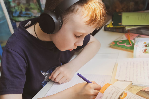 一个欧洲男孩在家里的桌子上做作业。一个戴着耳机的学生正坐在笔记本电脑前。与隔离有关的家庭作业和远程学习。图片下载