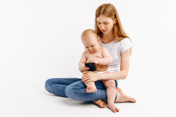 妈妈和她的小宝宝在白色背景下使用智能手机，面带微笑图片下载