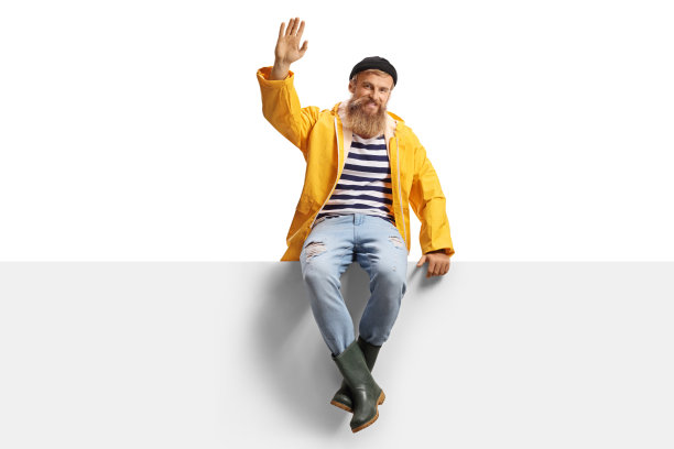 长满胡子的渔夫，穿着一件黄色雨衣，坐在一块嵌板上挥着手图片下载