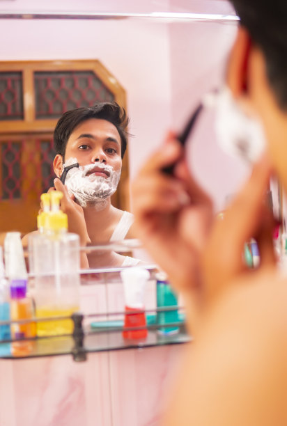 印度年轻人在家对着镜子刮胡子。图片下载