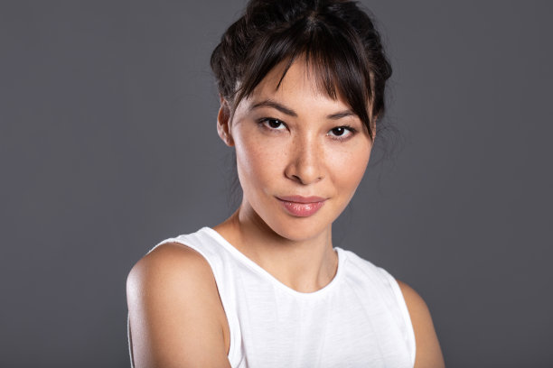 年轻的亚洲美丽女人的特写与笑脸在灰色的背景。图片下载