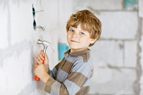 一个小男孩在工地上帮忙拿玩具工具。6岁的有趣的孩子，在建立新的家庭的乐趣。拿着钉子和锤子的孩子。图片下载