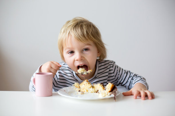 可爱的蹒跚学步的孩子，吃一块蛋糕和喝果汁图片下载