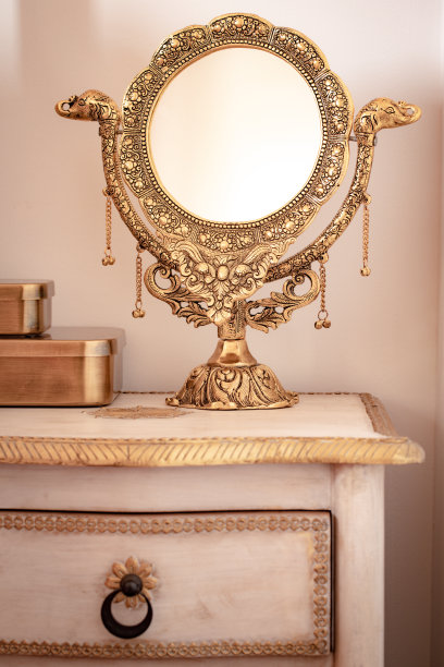 一面装饰精美的金色镜子放在时髦的床头柜上。女性的优雅，暖色图片下载