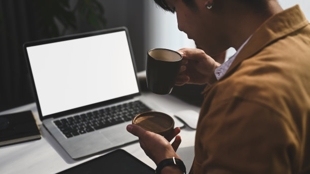 一个年轻的自由职业者坐在他的电脑前，喝着热咖啡。图片下载