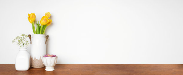 架子上的家居装饰。花瓶上有郁金香和肉质植物。靠在白墙上的木架。图片下载