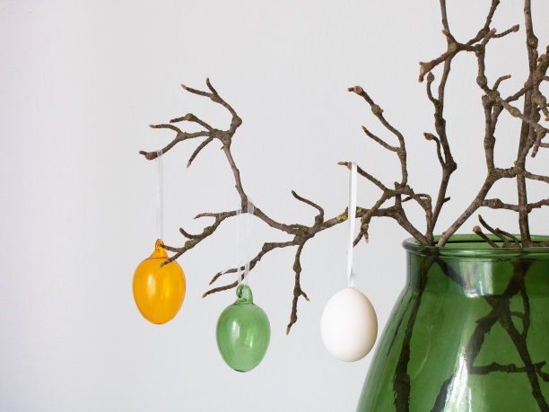 一张木兰花干枝的特写，上面挂着三个鸡蛋形状的玩具，橙色、绿色、白色。复活节卡片的概念图片下载