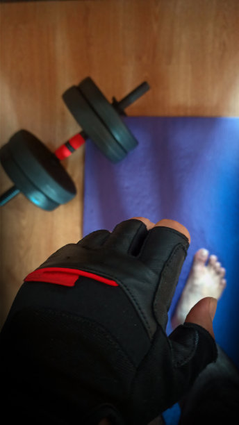 在家工作的概念显示俯视图举重手手套与一个人站在蓝色氯丁橡胶垫旁边的手举哑铃。图片下载