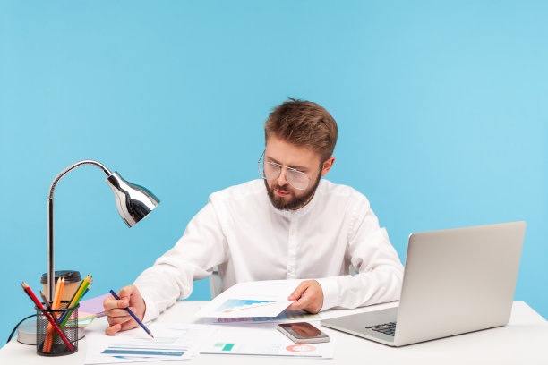 一个穿着白衬衫的专注的商人，在工作场所用笔记本电脑查看和分析信息图片下载