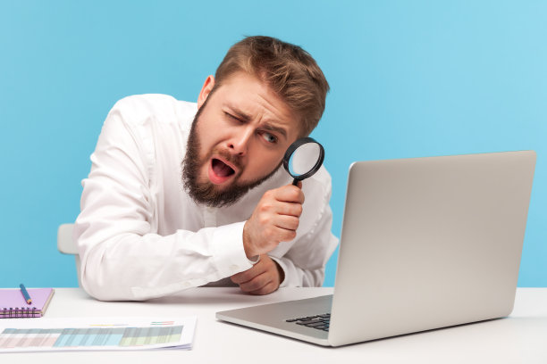 好奇的上班族通过放大镜看笔记本电脑的显示，试图找出私人安全信息，控制互联网连接图片下载