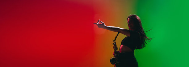 年轻女孩的剪影与萨克斯摆姿势孤立在绿色红色的背景。图片下载