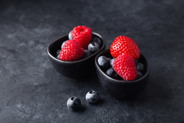 新鲜的浆果装在黑色的小碗里，背景是黑色的石头图片下载