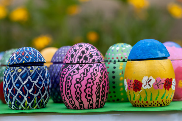 在黄色和橙色的春花前，一个绿色的底座上放着手工制作的复活节彩蛋图片下载