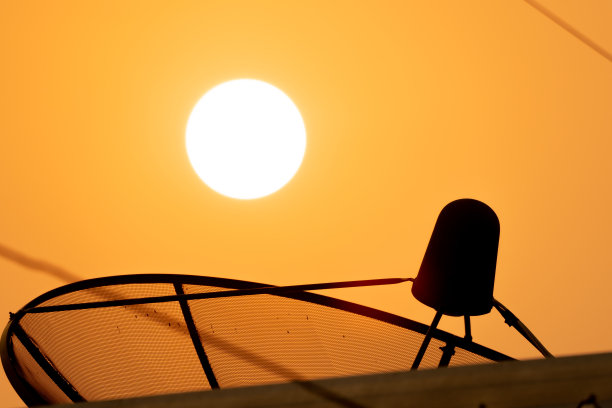 卫星技术碟式接收器在日出和金色的天空背景下，模糊的屋顶前景在阳光的光线图片下载