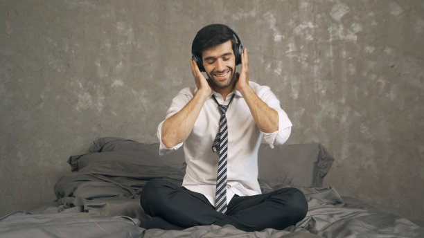 中东商人的肖像，CEO戴着耳机在床上跳舞，卧室里用手机听音乐。娱乐休闲的乐趣。人们在家里的生活方式。图片下载