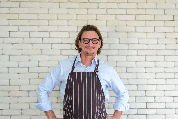 快乐的高级男子园艺肖像戴眼镜和牛仔围裙站在白色砖的背景与自由空间或文本复制空间。看相机。图片下载