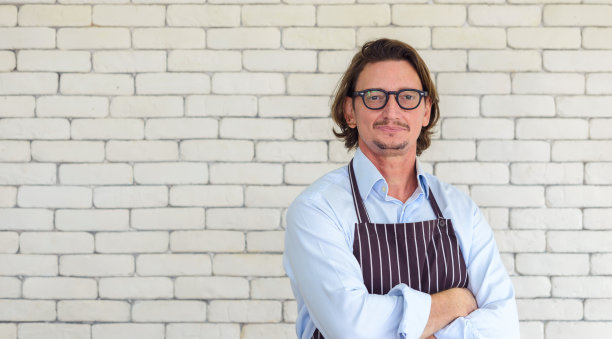 快乐的高级男子园艺肖像戴眼镜和牛仔围裙站在白色砖的背景与自由空间或文本复制空间。看相机。图片下载