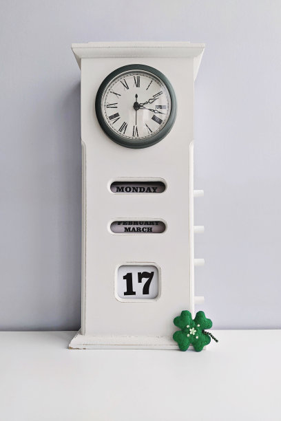木制的白色古董时钟与日历和圣帕特里克节三叶草在灰色背景图片下载
