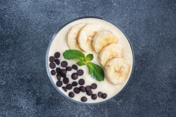 健康的早餐，甜点，牛奶酸奶香蕉和巧克力在一个盘子里。黑暗的具体背景。俯视图，复制空间。图片下载