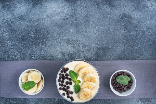 健康的早餐，甜点，牛奶酸奶香蕉和巧克力在一个盘子里。黑暗的具体背景。俯视图，复制空间。图片下载
