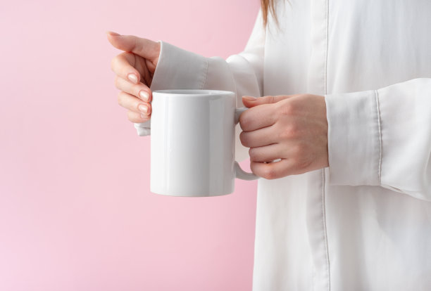 模型的白色咖啡杯或马克杯在女性手中粉红色的背景与复制空间。空白模板为您的设计，品牌，业务。真实的照片。女衬衫休闲风格图片下载