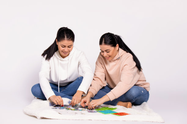 双胞胎女孩热情地在地板上收集拼图。一个有趣的消遣。图片下载