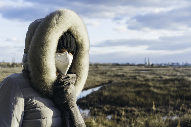 忧心忡忡的妇女戴着防护口罩和冬衣，草原荒野和工厂的背景-行动主义和环保理念-污染理念图片下载
