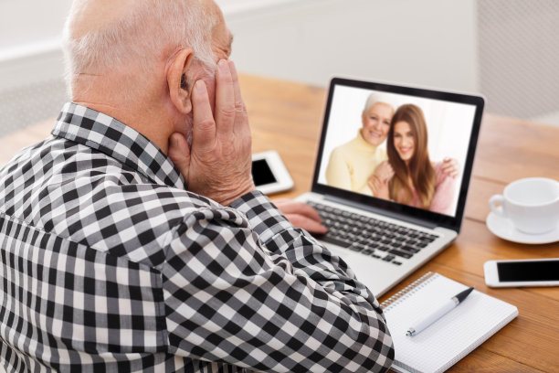 一位老人在室内用笔记本电脑与他的妻子和女儿进行远程交流图片下载