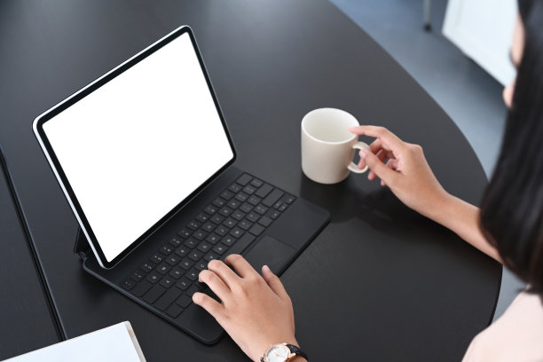 这是一位女商人拿着咖啡杯在办公桌上用平板电脑工作的照片。图片下载