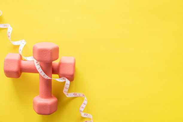 黄色背景上的哑铃和卷尺。健身、运动和锻炼图片下载