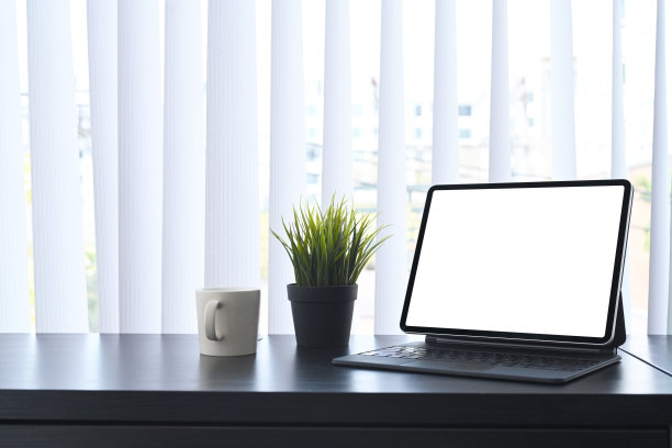 窗边的黑色桌子上放着电脑、植物和咖啡杯。图片下载