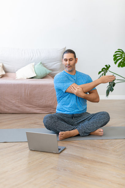 一个中年男子在网上蒸的垂直照片。在家锻炼-锻炼前拉伸肌肉图片下载