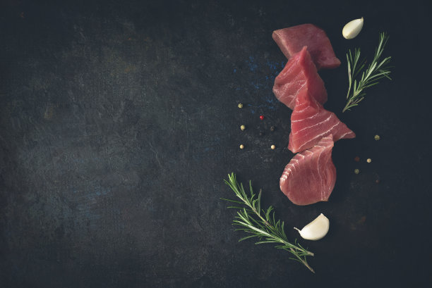 新鲜的红色金枪鱼切片与迷迭香，大蒜和胡椒烧烤或烹饪在黑暗的复古背景，平面设计或文本复制空间，俯视图图片下载